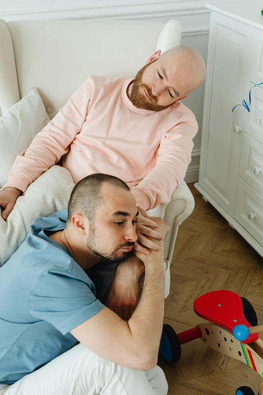 a man sitting on top of a couch next to a baby, by Julia Pishtar, trending on reddit, romanticism, two men hugging, bald head, laying in bed, disappointed