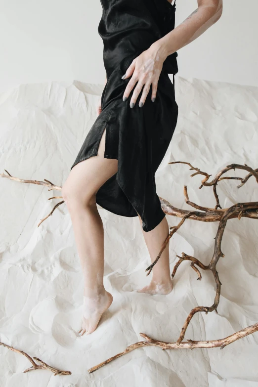 a woman in a black dress standing on a bed, by Caro Niederer, trending on unsplash, renaissance, laying on sand, unfinished roots of white sand, detailed shot legs-up, soft silk dress