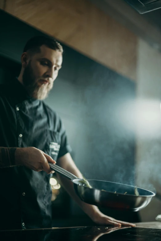 a man standing in a kitchen preparing food, dark backdrop, light beard, sage smoke, lachlan bailey