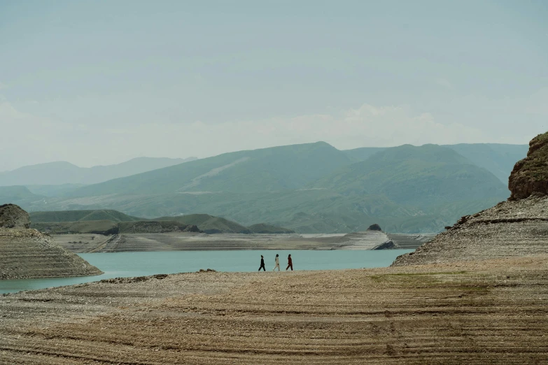 a couple of people that are standing in the dirt, by Muggur, pexels contest winner, land art, a lake between mountains, georgic, still from l'estate, people walking in the distance