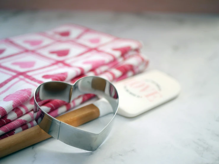 a heart shaped cookie cutter sitting on top of a table, by Sylvia Wishart, featured on pinterest, full product shot, white and pink cloth, metal kitchen utensils, square