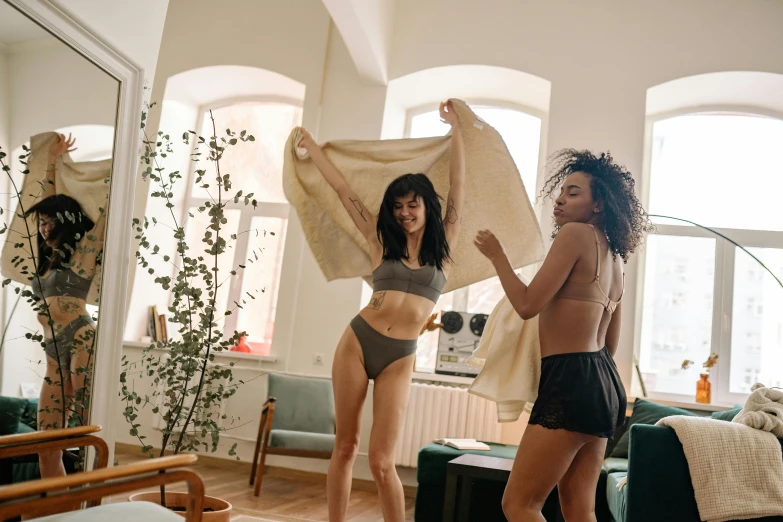 a couple of women standing next to each other in a living room, by Emma Andijewska, trending on pexels, happening, underwear ad, waving, wearing loincloth, working out