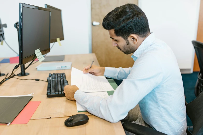 a man sitting at a desk in front of a computer, vastayan, writing on a clipboard, internal environment, thumbnail