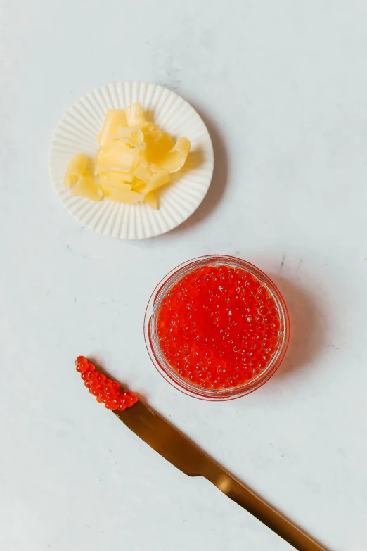 a knife sitting next to a bowl of red cavia, reddit, red caviar instead of sand, with sparkling gems on top, jelly - like texture, jen yoon