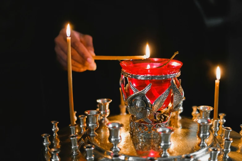a close up of a person lighting a candle, 👰 🏇 ❌ 🍃, orthodoxy, silver, crimson themed
