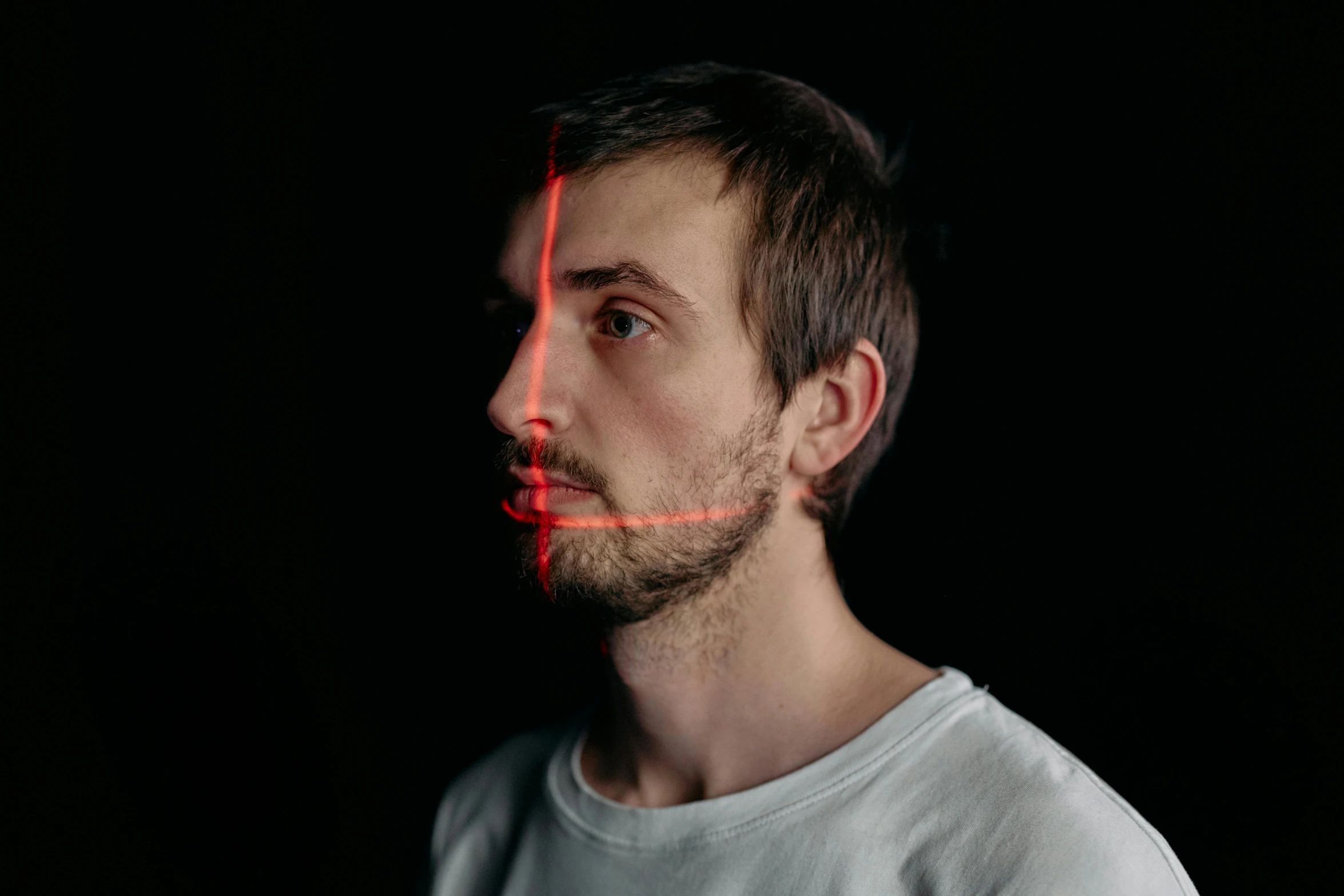 a man with a red light on his face, by Adam Marczyński, pexels contest winner, hyperrealism, red laser scanner, square jaw-line, looking to his side, half face