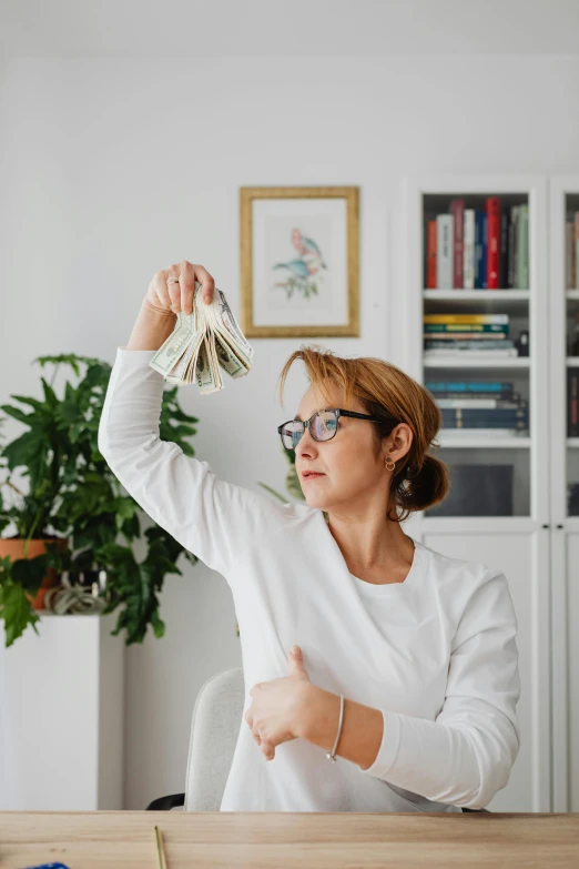 a woman sitting at a table with a bunch of money in her hand, pexels contest winner, modernism, raising an arm, balance, middle - age, instagram post