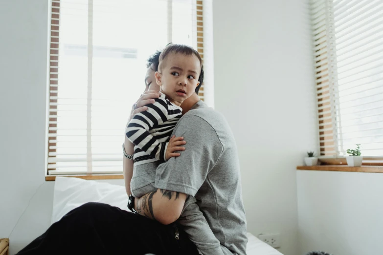 a woman sitting on top of a bed holding a baby, pexels contest winner, hurufiyya, over his shoulder, tattooed, 4yr old, bedhead