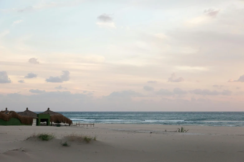 a couple of umbrellas sitting on top of a sandy beach, thatched roofs, at dawn, in socotra island, image from afar