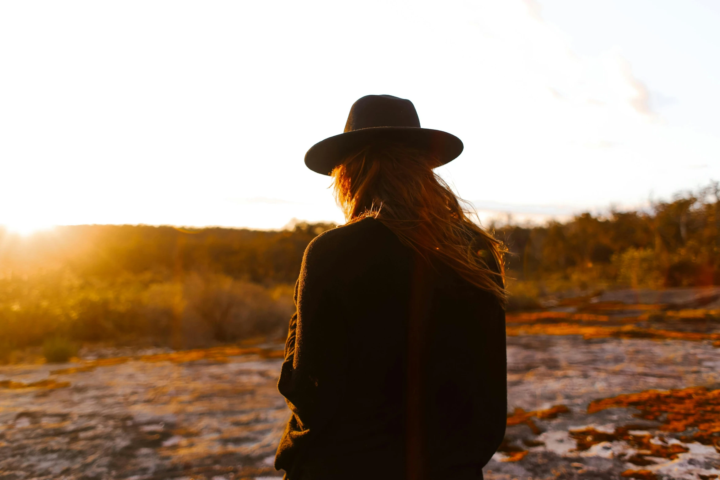 a woman wearing a hat standing in a field, pexels contest winner, australian tonalism, watching the sunset, profile image, flowy hair standing on a rock, black stetson hat