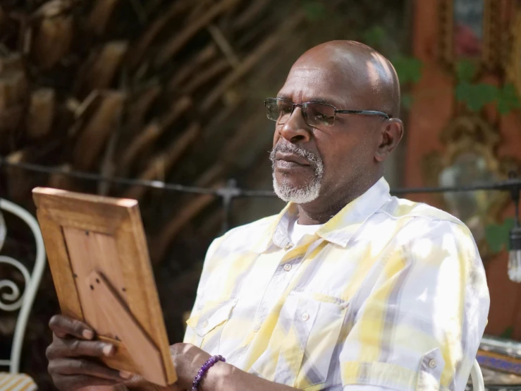 a man sitting at a table reading a book, inspired by George Barret, Sr., pexels contest winner, bahamas, holding a wood piece, on location, samuel jackson