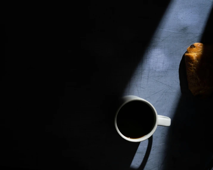 a cup of coffee and a croissant on a table, by Andrew Domachowski, unsplash contest winner, shadowy and dark, back lit, 15081959 21121991 01012000 4k, dark angel of coffee
