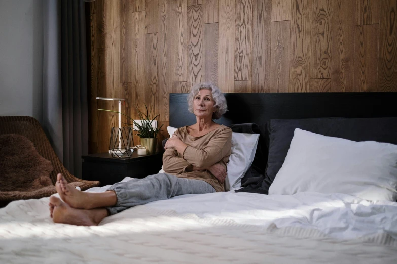 a woman sitting on a bed in a bedroom, pexels contest winner, photorealism, older woman, manuka, annoyed, award-winning render