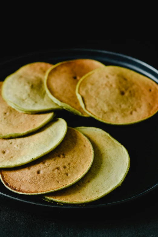 a black plate topped with pancakes on top of a table, product image, green gold, close up of iwakura lain, flat curves