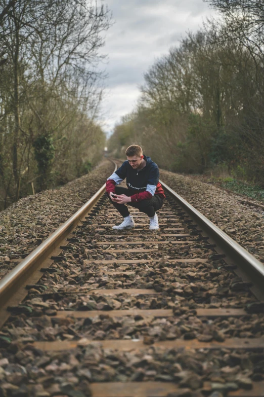 a man squatting down on a train track, an album cover, by Sam Charles, pexels contest winner, male teenager, low quality photo, conor walton, pr shoot