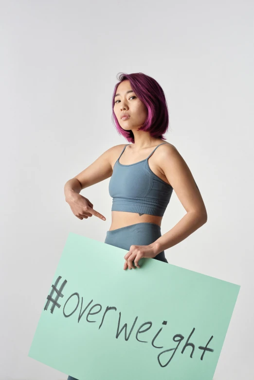 a woman holding a sign that says overweight, an album cover, inspired by helen huang, trending on pexels, feminist art, with teal clothes, training bra, beauty campaign, arms out