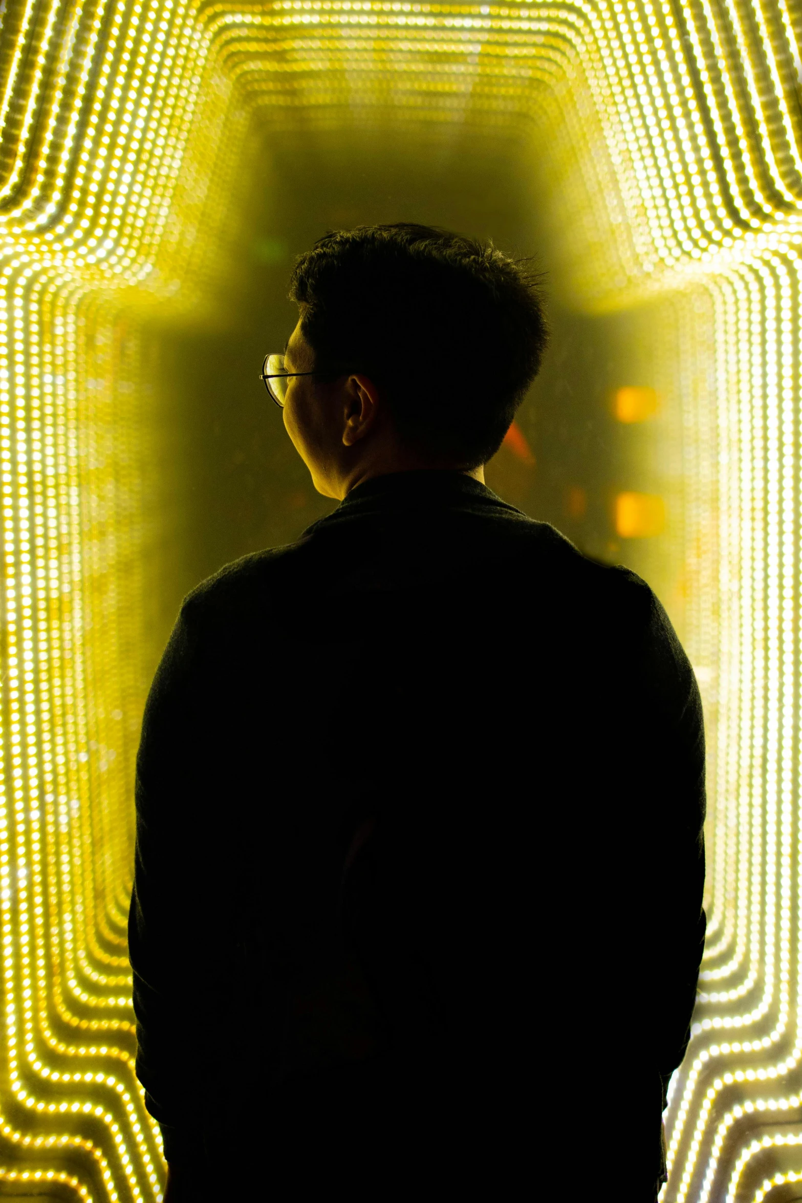 a man standing in front of a light tunnel, yellow lights, infinity mirror, asian male, man with glasses