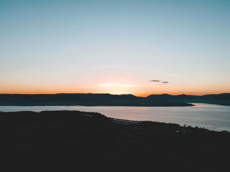 the sun is setting over a large body of water, pexels contest winner, hills in the background, birdseye view, views to the ocean, split near the left