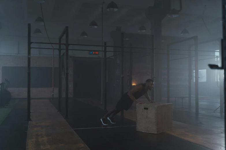 a man standing next to a box in a room, a 3D render, inspired by jessica rossier, realism, athletic crossfit build, at night, local gym, volume raytracing fog