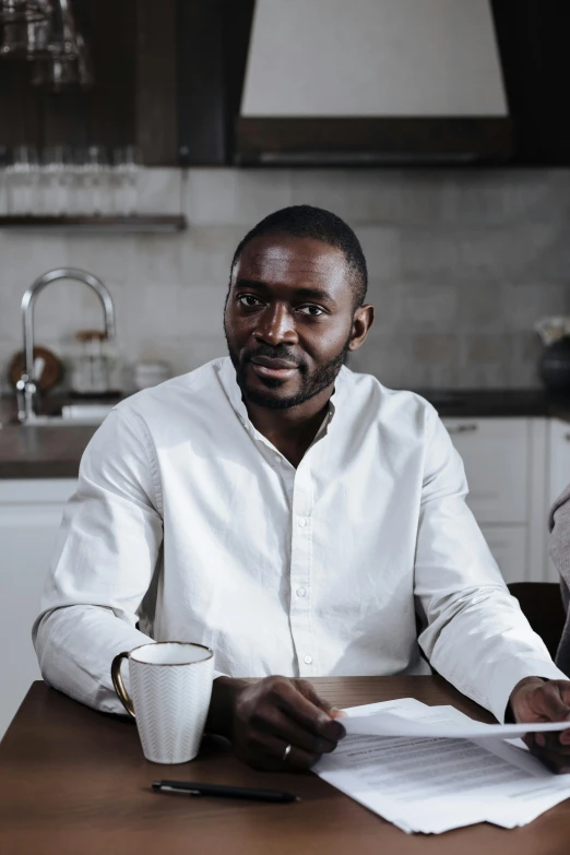 a man sitting at a table in front of a laptop, a portrait, inspired by Rajmund Kanelba, pexels contest winner, white dress shirt, in the kitchen, on grey background, adebanji alade