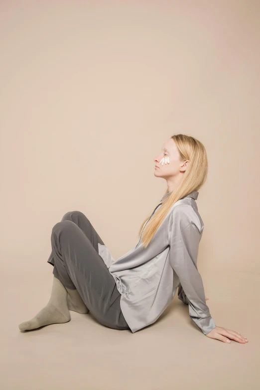 a woman sitting on the floor with her legs crossed, by Maud Naftel, unsplash, grey clothes, silky garment, wearing a track suit, with long blond hair