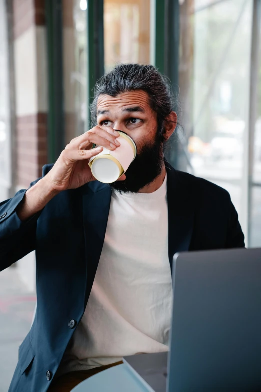 a man sitting in front of a laptop drinking from a cup, pexels contest winner, renaissance, aboriginal australian hipster, man in black suit, unkempt hair and beard, official screenshot