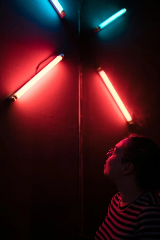 a person standing in front of a wall with neon lights, by Doug Ohlson, red light bulbs, tubes, photographed for reuters, red light saber