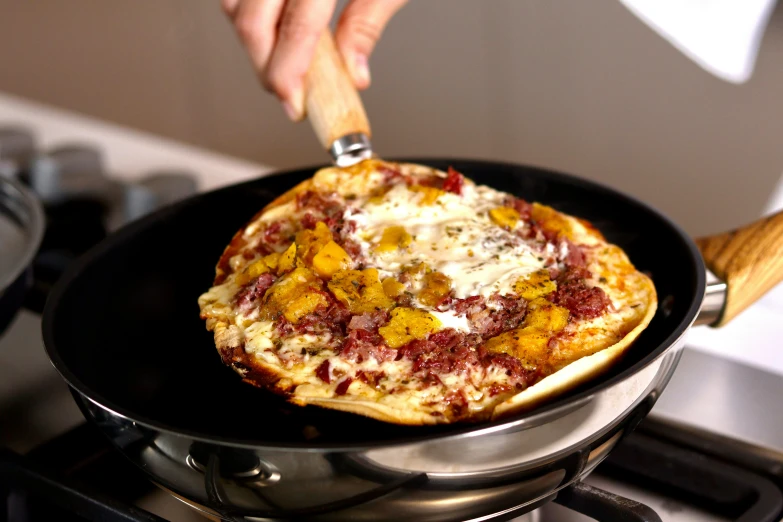 a person cooking a pizza in a pan on a stove, mango, bedhead, easy to use, with ornate jewelled