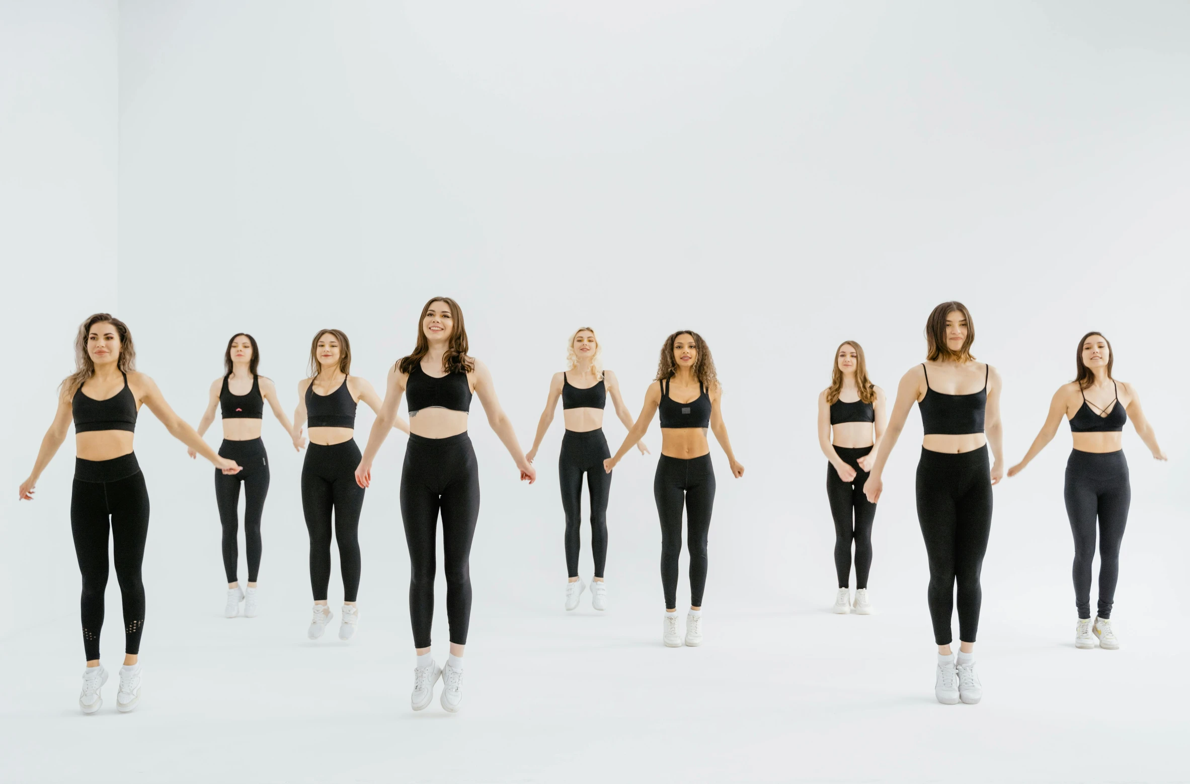 a group of women standing in front of a white wall, trending on pexels, antipodeans, black leggins, choreographed, animation, rendering of beauty pageant