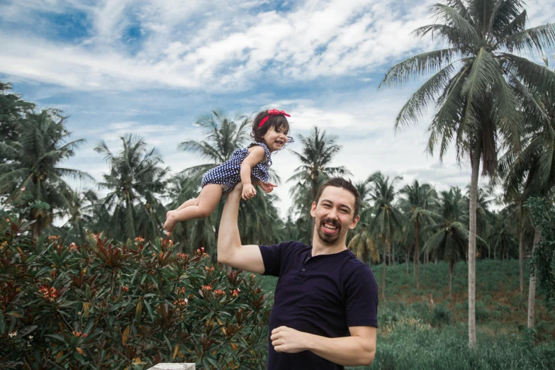 a man holding a little girl up in the air, a portrait, pexels contest winner, palm trees in the background, avatar image, in style of lam manh, belle delphine