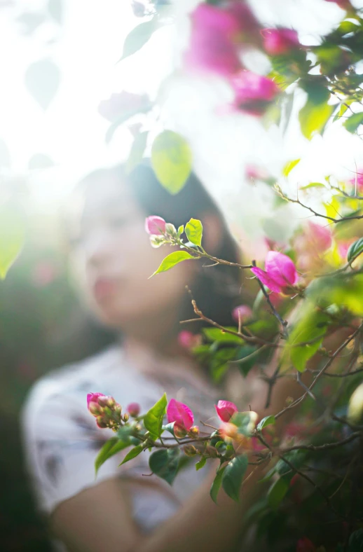 a woman standing in front of a bush of flowers, inspired by Jung Park, unsplash, softly backlit, portrait of mulan, spring light, thoughtful