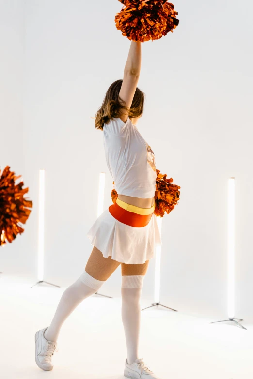 a woman holding up a bunch of pom poms, by Gavin Hamilton, trending on unsplash, light and space, white and orange breastplate, nfl, light lighting side view, hip skirt wings
