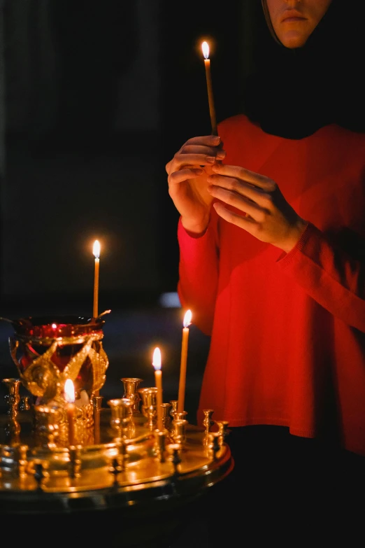 a woman lighting a candle in a church, by Julia Pishtar, trending on unsplash, red and gold cloth, holding wands, serene lighting, traditional