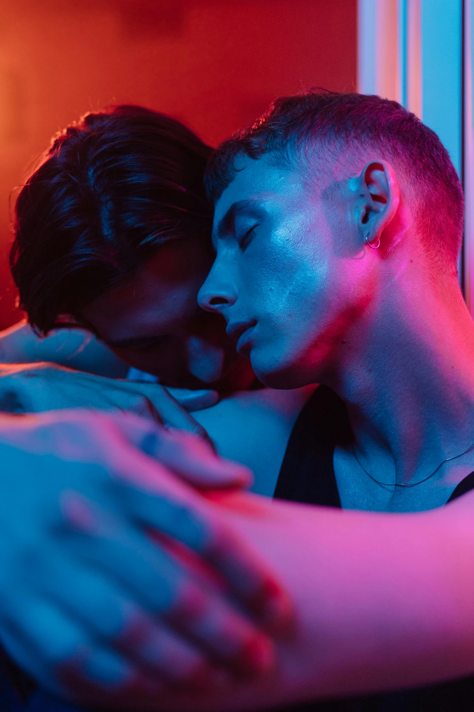 a man and a woman hugging in front of a window, inspired by Nan Goldin, trending on pexels, blue and red lights, two young men, multi - coloured, steven klein