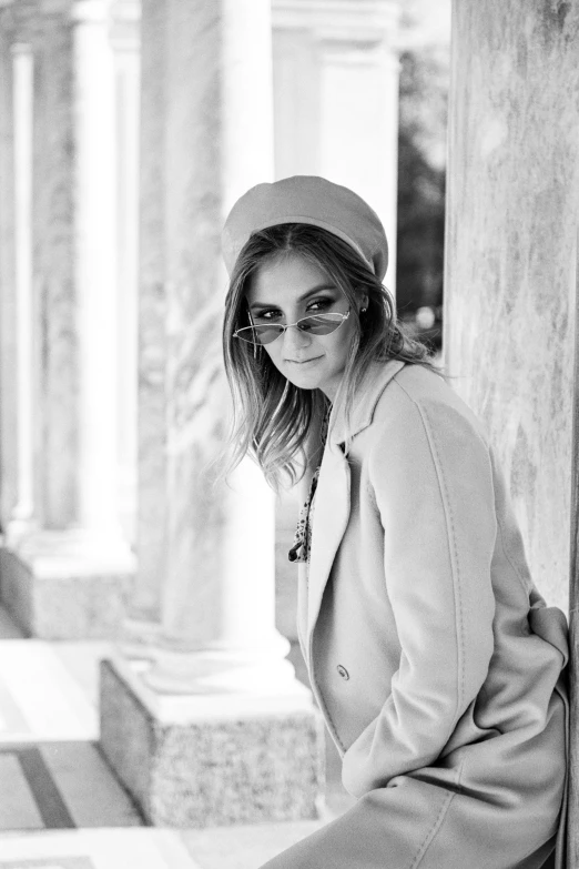 a black and white photo of a woman leaning against a column, beret and sunglasses, in style of britt marling, wearing a fancy jacket, sofya emelenko