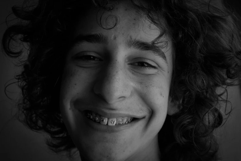 a black and white photo of a man with curly hair, by Kristian Zahrtmann, pexels contest winner, humanoid with crooked teeth, 14 yo berber boy, detailed realistic smiling faces, teenage girl