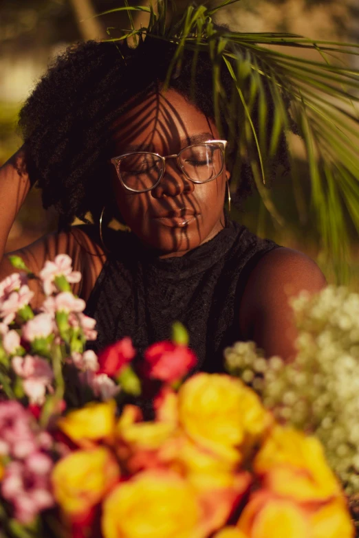 a woman holding a bunch of flowers in front of her face, an album cover, by Dulah Marie Evans, trending on unsplash, afrofuturism, square rimmed glasses, sitting with flowers, lush surroundings, black black black woman