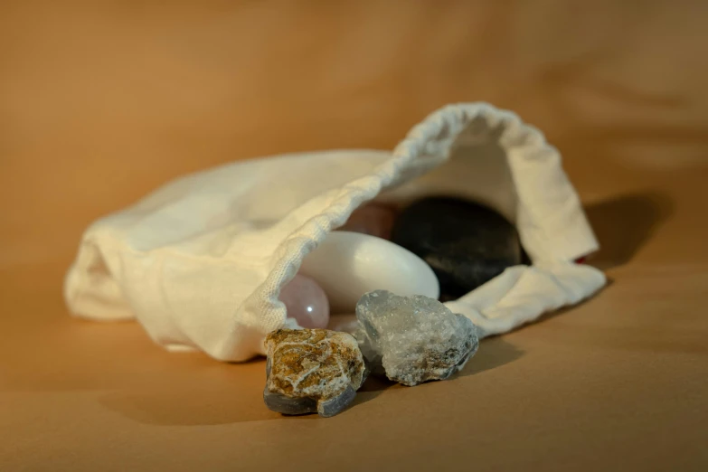a bag filled with rocks sitting on top of a table, a marble sculpture, by Helen Stevenson, unsplash, white and pink cloth, healing tubes, close-up product photo, amber