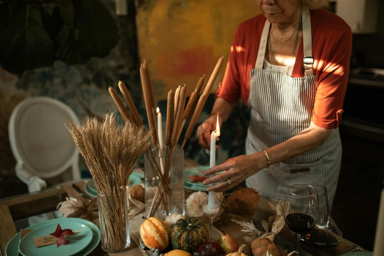 a woman standing in front of a table filled with food, a still life, trending on pexels, process art, holding a candle holder, harvest, holding paintbrushes, baking french baguette