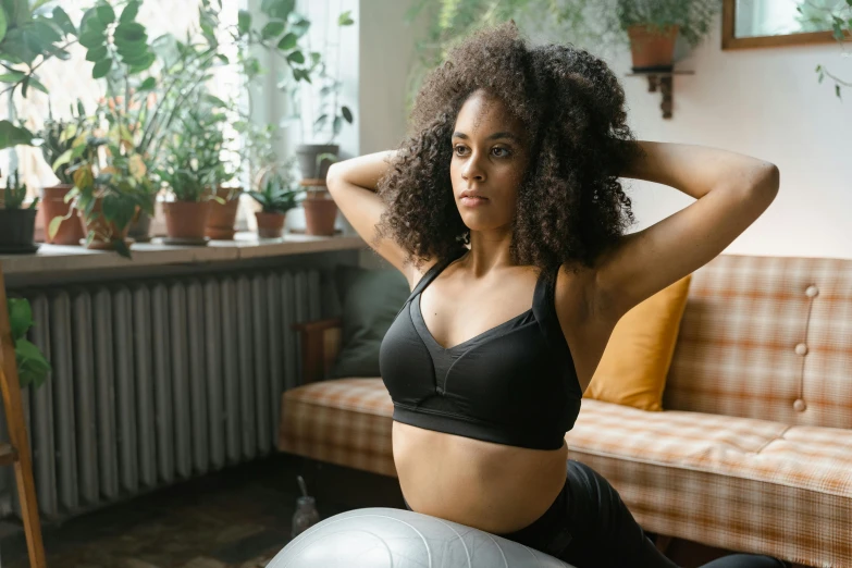 a woman sitting on an exercise ball in a living room, trending on pexels, detailed sports bra, black female, thumbnail, lush surroundings