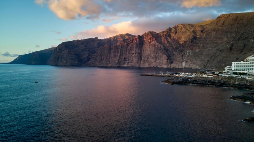 a large body of water with a mountain in the background, by Lee Loughridge, pexels contest winner, romanticism, coastal cliffs, last light, miguel iglesias, port