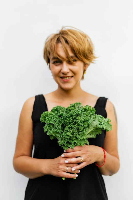 a woman holding a bunch of green vegetables, an album cover, by Jessie Algie, pexels contest winner, halfbody headshot, she is wearing a black tank top, rebecca sugar, headshot profile picture