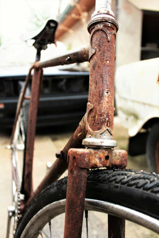an old rusty bike parked in front of a building, an album cover, assemblage, bottom body close up, restomod, bracts, ((rust))