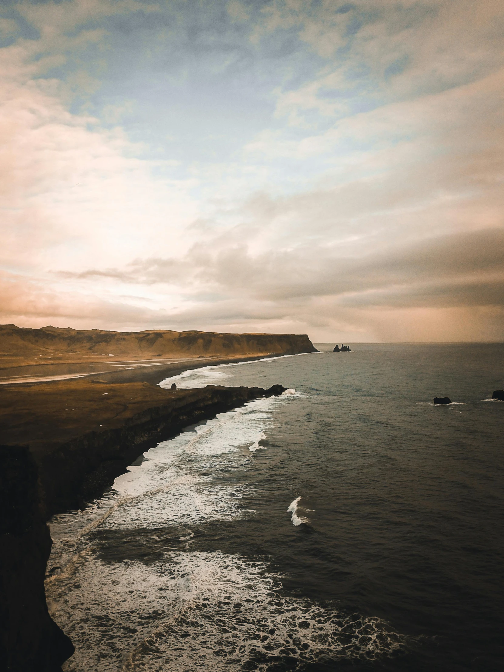 a large body of water next to a beach, by Johannes Voss, pexels contest winner, coastal cliffs, trending on vsco, islands on horizon, black sand