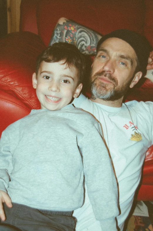 a man sitting next to a little boy on a red couch, a colorized photo, instagram, he also wears a grey beanie, zachary corzine, h3h3, parental advisory