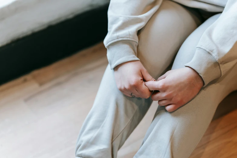 a woman sitting on the floor with her hands on her knees, by Nina Hamnett, trending on pexels, antipodeans, beige hoodie, holding hands, grey, wearing a track suit