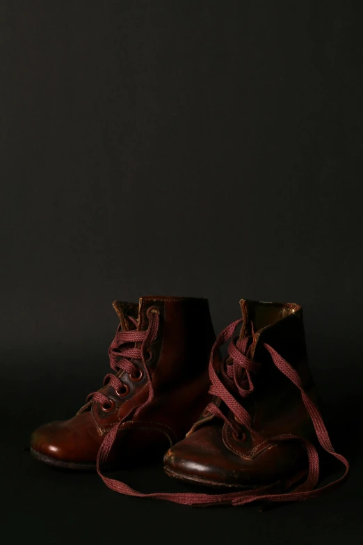 a pair of brown boots on a black background, a portrait, unsplash, photorealism, maroon red, studio medium format photograph, 1910s, high school