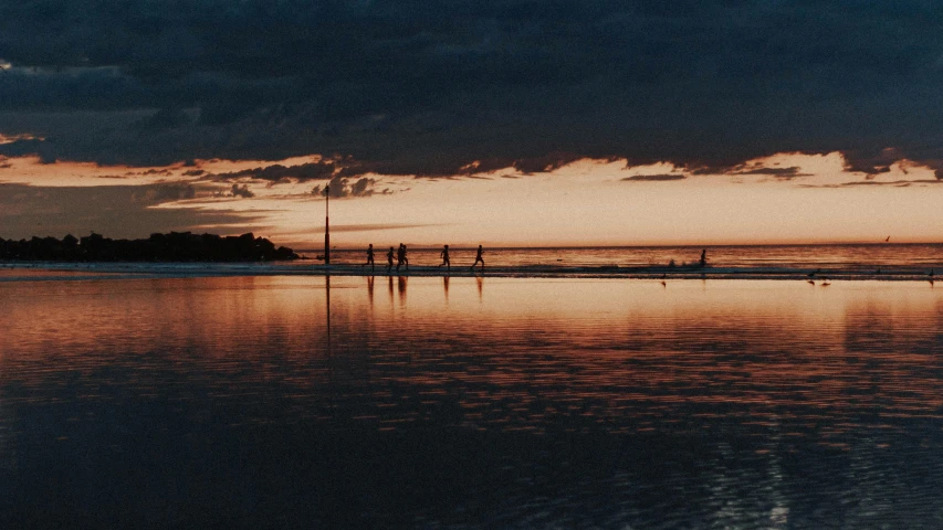 a group of people standing on top of a beach next to the ocean, by Carey Morris, unsplash contest winner, minimalism, reflections in copper, evening at dusk, australian beach, standing on the water ground