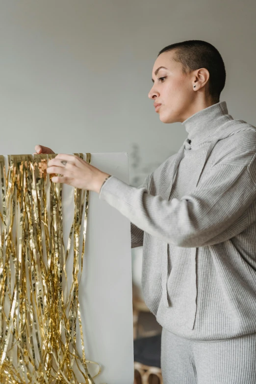 a woman standing in front of a gold curtain, trending on pexels, visual art, ribbons, on a gray background, crafting, wearing a fancy jacket