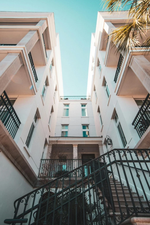 a staircase going up to the top of a building, inspired by Ricardo Bofill, pexels contest winner, neoclassicism, apartments, courtyard, bright sky, teal aesthetic